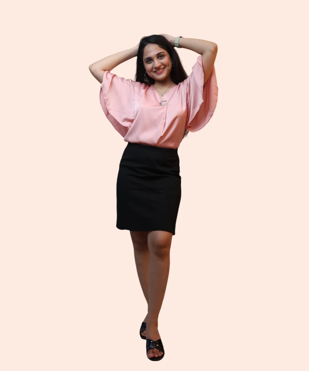 Full length women's baby pink satin cape sleeve V-neck blouse hands in hair playful workwear pose Ladymade