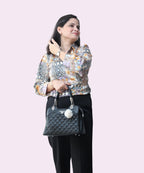 A woman posing in a multi-colored satin V-neck blouse with tribal patterns and a center brooch by Ladymade.