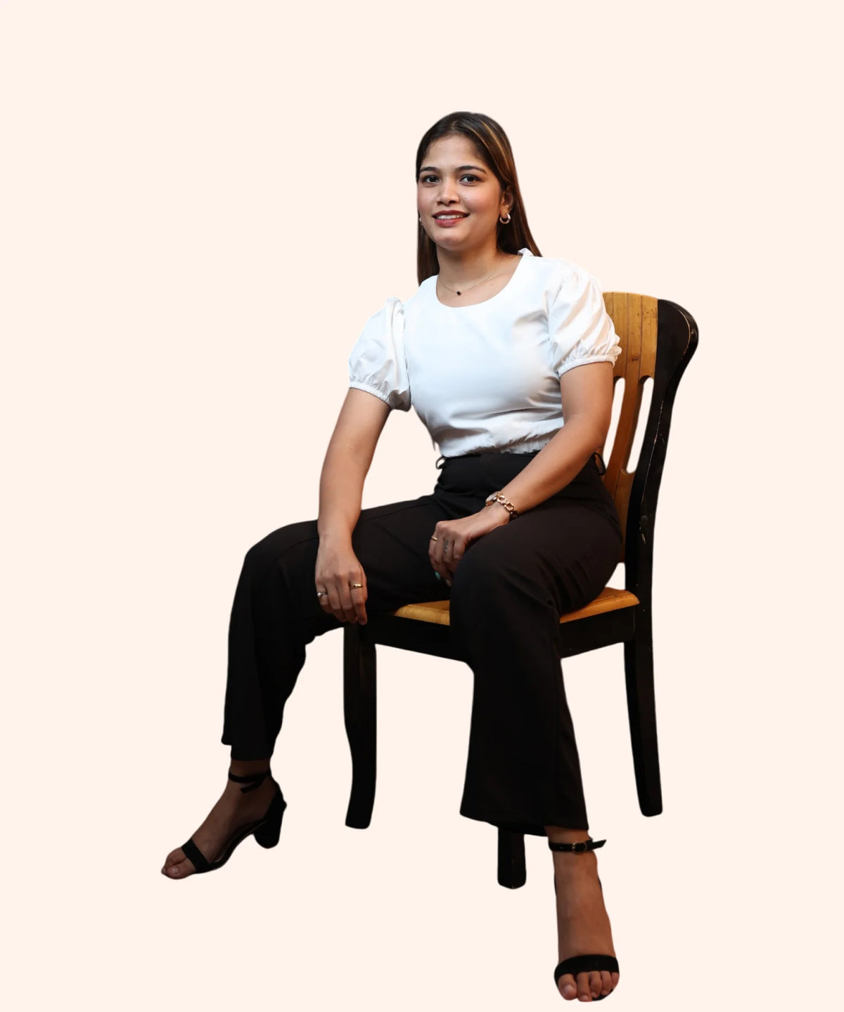 Full sitting profile of a woman modeling an off-white puff sleeve crop top on a wooden chair by Ladymade.