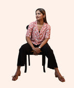 Full sitting view of a woman styling a peach pink daisy crop top with black trousers by Ladymade.