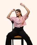 A woman smiling and posing while seated in a peach pink daisy print corporate shirt by Ladymade.
