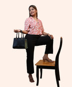 Full standing view of a woman holding a handbag in a peach pink floral workwear crop top by Ladymade.