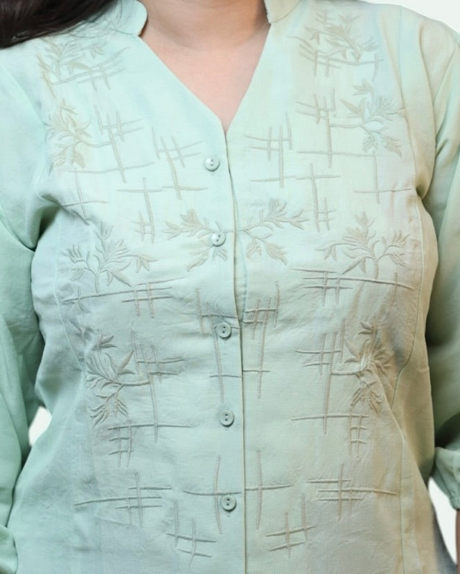 Close-up texture shot of the tonal geometric embroidery and buttons on a women's pista green cotton office top by Ladymade.