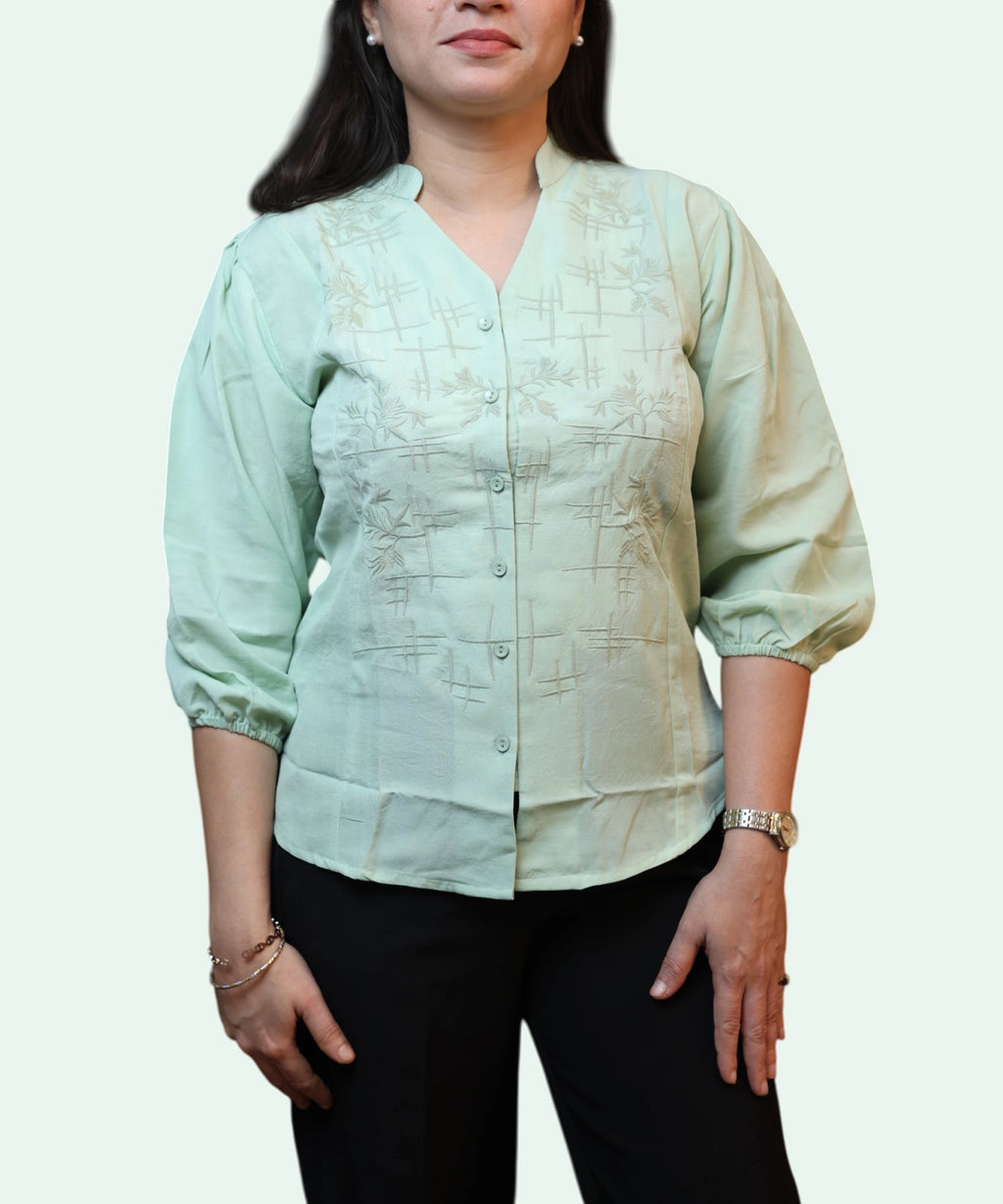 Three-quarter front view of a woman wearing a pista green cotton workwear blouse paired with black trousers by Ladymade.