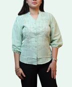 Three-quarter front view of a woman wearing a pista green cotton workwear blouse paired with black trousers by Ladymade.