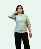 Three-quarter front view of a woman wearing a pista green cotton workwear blouse paired with black trousers by Ladymade.