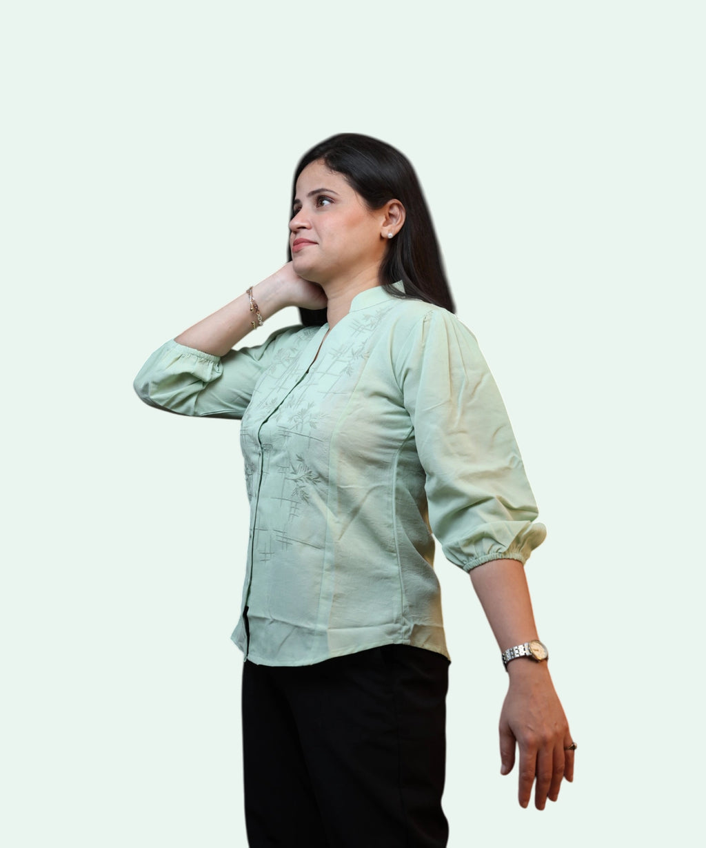 Close-up texture shot of the tonal geometric embroidery and buttons on a women's pista green cotton office top by Ladymade.