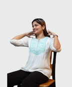 Women's white cotton kurti top turquoise floral embroidered yoke gathered silhouette seated smiling Ladymade